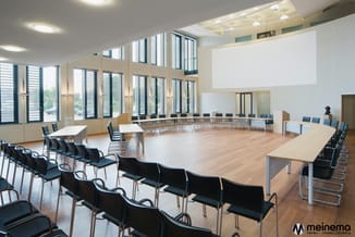 Moderne vergaderzaal met zwarte stapelstoelen, houten vergadertafels, grote ramen met jaloezieën, houten vloer en projections