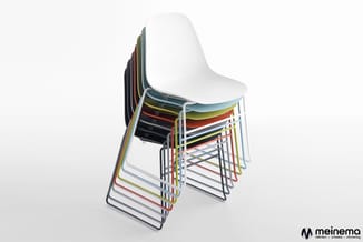 Gestapelde kunststof stoelen met metalen buisframe in verschillende kleuren (wit, zwart, rood, geel, grijs) tegen witte achte