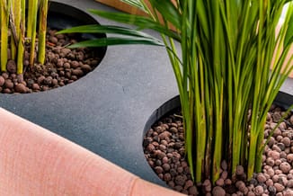 Grijs akoestisch scheidingspaneel tussen plantenbakken met bruine hydrokorrels en groene siergrassen in kantooromgeving.