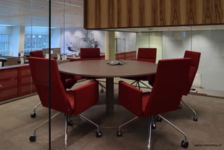 Moderne vergaderruimte met ronde tafel, vier rode kantelbare stoelen met wielen en glazen wanden. Houten plafond en betonnen