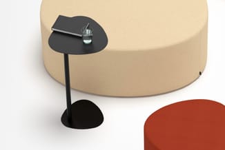 Beige ronde poef met zwart bijzettafeltje met glazen blad en waterglas, naast rood zitmeubel.