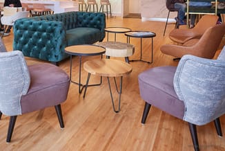 Loungehoek met paarse fauteuils, turquoise chesterfield bank en houten bijzettafels op houten vloer.