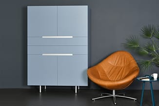 Blauwe garderobekast met schuifdeuren en witte grepen naast cognackleurige leren fauteuil en bijzettafel in moderne kantoorru