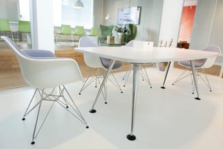 Witte vergadertafel met grijze poten en vier witte ergonomische stoelen met grijze zitting in modern kantoor met glazen wande