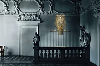 Klassieke interieurruimte met gouden hanglamp, zwart balkon, witte ornamentale plafonddetails en zwarte sculpturen tegen lich