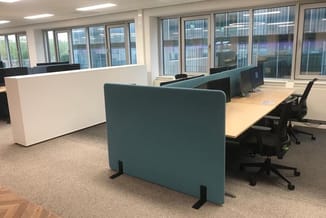 Kantoorruimte met teal akoestische schermen, houten bureau, zwarte ergonomische stoelen en witte receptiebalie bij ramen.