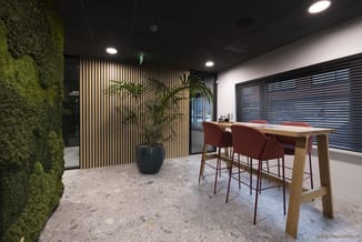 Modern kantoor met houten bartafel, bordeaux barkrukken, groene muswand, houten latten wand, potplant en horizontale jaloezie