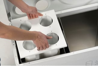 Persoon plaatst witte akoestische panelen met circulaire openingen in plafondframe van kantoorruimte.