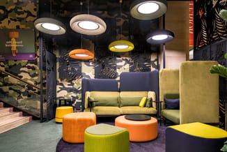 Moderne lounge met gele en groene zitbanken, oranje en groene poufzit, hangende LED-lampen in oranje en geel, zwart-witte bla