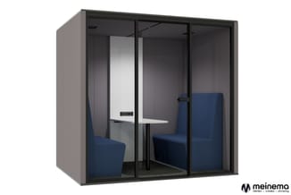 Gesloten belcel met donkergrijs frame, glazen wanden, witte tafel, twee blauwe stoelen en grijze vloer.
