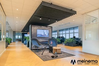 Modern kantoorlobby met loungehoek: twee blauwe stoelen rond houten tafel, TV-scherm aan muur, akoestische plafondpanelen, ho