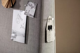 Grijze stofwand met bevestigde witte notities, houten wanddecoratie en beige vilten organizer met pennen.