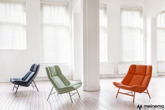Drie moderne loungestoelen in zwart, groen en oranje in een licht kantoorinterieur met witte zuilen, houten vloer en grote ra
