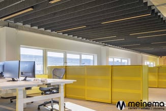 Modern kantoor met gele akoestische scheidingswanden, wit bureau met monitoren, ergonomische stoel en plafondverlichting met