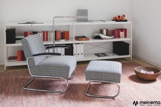Moderne werkruimte met witte boekenkasten vol rode en oranje boeken, zwart-wit gestoffeerde fauteuil en poef met metalen fram