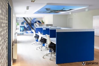 Modern kantoor met blauwe werkwanden, witte ergonomische stoelen, grijze werkbladen, geometrisch wandpaneel en luchtzicht pla