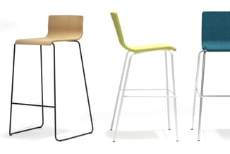Drie moderne barkrukken: houten zitting op zwart metalen frame, gele stof op wit frame, en groenblauwe stof op zilver metaal