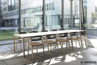Moderne vergadertafel met witte blad en houten onderstel, omringd door houten stoelen met zwarte zitting in groot, licht kant
