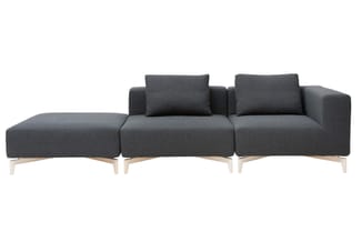 Grijze modulaire bank met chaise longue links, twee zitplaatsen met rugkussens en natuurhouten poten op witte achtergrond.