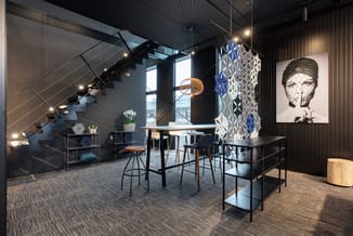 Modern kantoor met zwarte werkafels, houten zitjes, metalen trappenhuizen, geometrische wandpanelen en portretkunstwerk aan w
