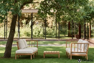 Houten loungestoelen met witte kussens en bijzettafel op grasveld onder boom, glazen gebouw op achtergrond.