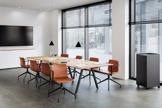 Moderne vergaderzaal met lange houten tafel, oranje stoelen met zwart frame, zwarte hangllampen, grote ramen met jaloeziën, T