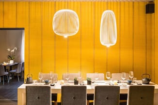 Moderne eetkamer met gele wandbekleding, witte hanglampjes, houten tafel en grijze stoelen in een kantoorruimte.