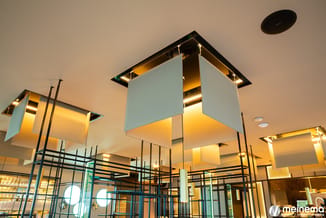 Moderne kantoorruimte met hangende lichtobjecten in wit en goud, zwarte metalen raamwerk en glazen wanden, warm verlicht plaf