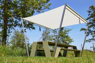 Beige tuinpaviljoen met wit zonnescherm en groen picknickset in buitenruimte onder bomen.
