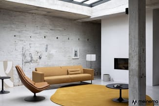 Moderne kantoorruimte met gele ronde tafel, geel-grijs linnen sofa, cognackleurige leunstoel, betonnen zuilen, witte bakstene