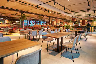 Modern kantoorruimte met houten vergadertafels, grijsblauwe stoelen, hangende verlichting en houten plafond.