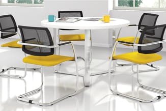 Ronde witte vergadertafel met zwarte mesh-stoelen met gele zittingen op wielen, in moderne kantoorruimte met ramen.