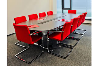 Moderne vergadertafel met rode conferentiestoel in kantoor met grote ramen en grijze vloer.