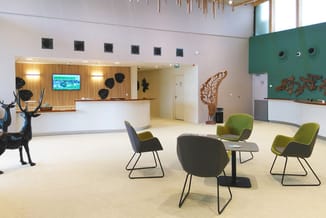 Modern kantoorlobby met receptie, groene en zwarte loungestoelen, houten wandelementen, hert sculptuur en groen accent wall.