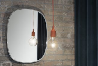Twee hangende verlichting met terracotta-kleurige fittingen en glazen bollen boven een ovale wandspiegel tegen een bakstenen