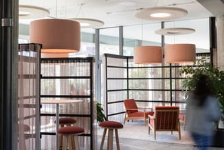 Modern kantoor met akoestische hangende schermen in beige, zwarte gridscheidingen, rode stoelen en houten accenten.