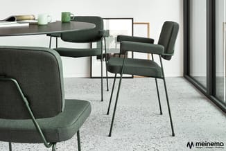 Moderne kantoorruimte met groene stoelen, ronde tafel en sofa in grijsgroen textiel, betonvloer, grote ramen.