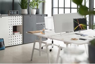 Modern kantoorwerk­station met witte bureau's, grijze opbergkast met perforatie, witte bureaustoelen, monitors en groene kant