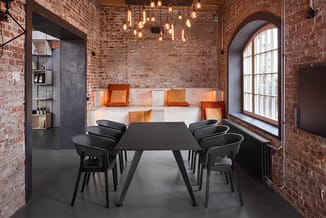 Moderne vergaderruimte met zwarte tafel, grijze stoelen, bakstenen wanden, oranje kussens op ingebouwde bank en hangende glaz
