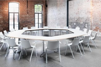 Witte moderne vergadertafel met organische vorm, omgeven door lichtgrijze stoelen in industriële lofruimte met bakstenen mure
