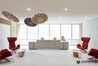 Modern receptie met rood gevormde fauteuils, betonnen balie, houten accenten, hangdecoratie en grote raampartij.
