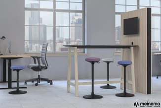Moderne kantoorruimte met houten stafel, zwarte werkblad, drie krukken met gekleurde zittingen, ergonomische bureaustoel, en