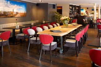 Modern kantoor-ontmoetingsruimte met houten vergadertafel, rode stoelen met grijze zitting, crème gekleurde zitbank en bar op
