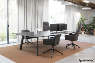 Moderne vergaderruimte met zwarte tafel, grijze stoelen met wieltjes, beige vloerkleed, raampartijen met gordijnen en groene