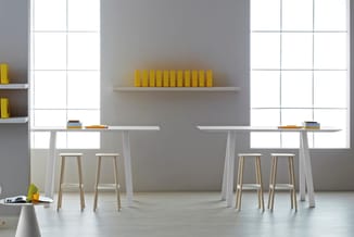 Moderne kantoorruimte met twee witte werkplekken, houten barkrukken, gele boeken op wandplank en grijze wand met grote ramen.