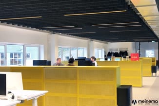 Moderne kantoorwerkplek met gele akoestische schermen, zwart plafond met ingebouwde verlichting, witte muren en grote ramen.