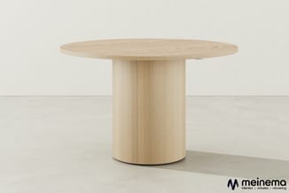 Ronde houten tafel met licht eiken finish en cilindervormig onderstel, tegen lichte achtergrond.