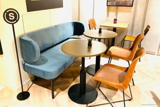 Showroom opstelling met blauwe gebogen bank, twee ronde tafels met zwart onderstel, bruinleren stoelen en houten stoelen tege