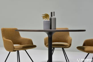 Zwarte ronde tafel met grijze blad, drie goudkleurige stoelen met zwarte poten, decoratieve fles en plantenpot bovenop.