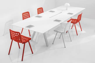 Vergadertafel in wit met grijze poten, omgeven door rode en witte perforeerde stoelen. Op tafel liggen tablets verdeeld. Witt